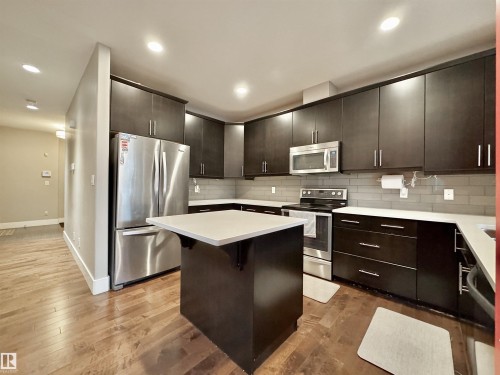 Kitchen featuring dark wood-finish cabinetry, stainless steel appliances, light countertops, and a gray tile backsplash - 3254 Allan Way, Edmonton, AB 