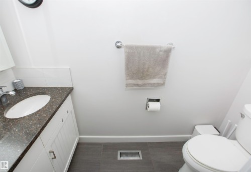 Bathroom featuring a white vanity with panel-front cabinetry, dark speckled countertop, and an undermount sink - 52 Mohawk Crescent, Leduc, AB 