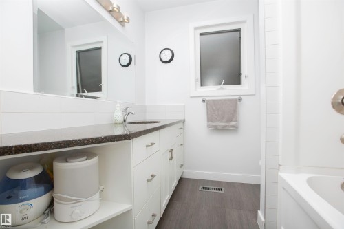 Bathroom featuring a white vanity with extensive storage, dark speckled countertop, single basin sink, and wood-finish flooring - 52 Mohawk Crescent, Leduc, AB 