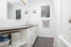 Bathroom featuring a white vanity with extensive storage, dark speckled countertop, single basin sink, and wood-finish flooring - 