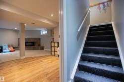Staircase with dark carpeting and white handrail leading to a lower level featuring wood-finish flooring, recessed lighting, and a stone-clad fireplace - 
