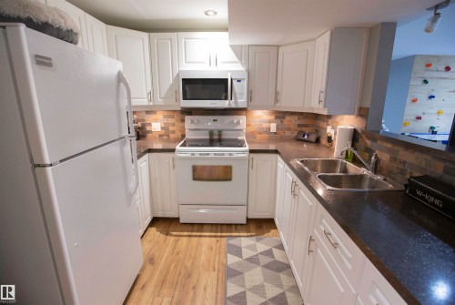 U-shaped kitchen featuring white cabinetry with silver hardware, dark countertops, a mosaic tile backsplash, and wood-finish flooring - 52 Mohawk Crescent, Leduc, AB 