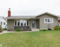 Ranch-style exterior featuring sage green siding, a brick chimney, and a bay window with stone accenting - 52 Mohawk Crescent, Leduc, AB 
