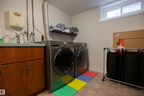 Laundry room featuring a utility sink with a laminate countertop, wood-finish cabinetry, and ceramic tile flooring - 52 Mohawk Crescent, Leduc, AB 
