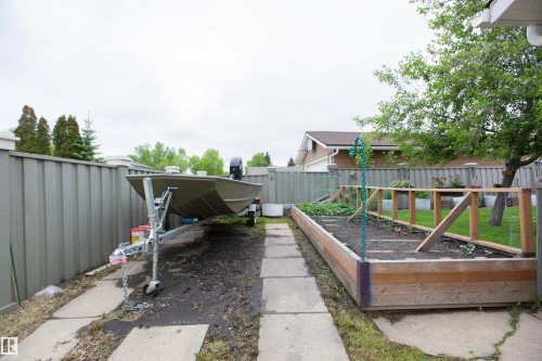 Backyard featuring a concrete paver pathway, wood-sided raised garden bed, and mature trees - 52 Mohawk Crescent, Leduc, AB 