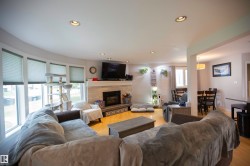 Spacious living area featuring light wood-finish flooring, a contemporary fireplace with a stone surround, and recessed ceiling lighting - 