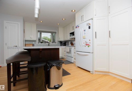 Bright kitchen featuring light wood-finish flooring, white cabinetry, recessed lighting, and a kitchen island with a light-colored countertop - 52 Mohawk Crescent, Leduc, AB 