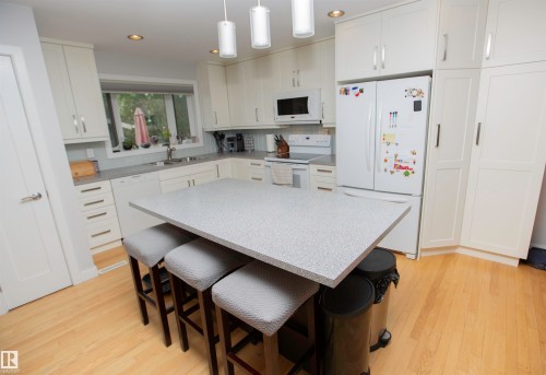 Kitchen featuring a central island with seating for three, white cabinetry, light countertops, wood-finish flooring, and recessed lighting - 52 Mohawk Crescent, Leduc, AB 