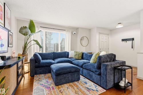 Light-filled living area featuring wood-finish flooring, large windows with white curtains, a white paneled door, and ceiling-mounted lighting - 14807 141 Street, Edmonton, AB 
