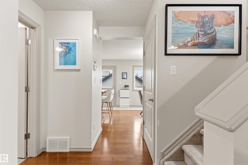Interior hallway featuring wood-finish flooring, light neutral wall paint, white trim, and a carpeted staircase - 14807 141 Street, Edmonton, AB 