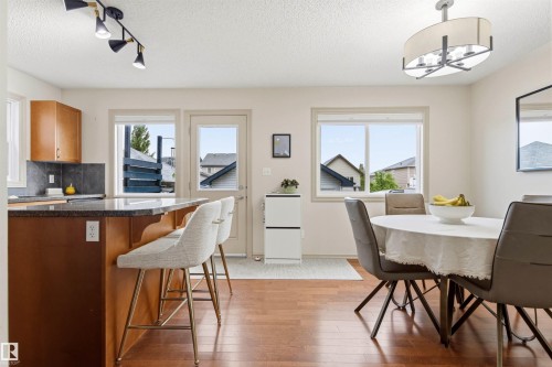 Open-concept living space with wood-finish flooring, a kitchen island featuring a granite-look countertop, wood cabinetry, and a dark tile backsplash - 14807 141 Street, Edmonton, AB 