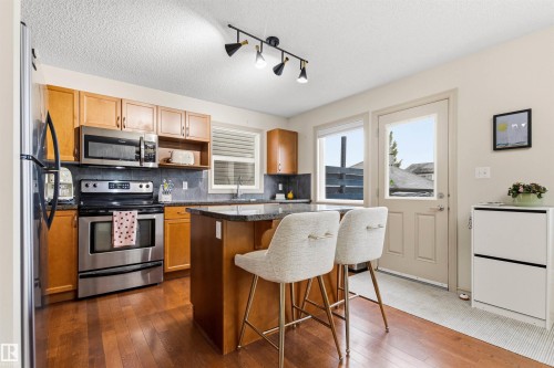 Kitchen featuring wood-finish flooring, light wood cabinetry, stainless steel appliances, and a central island with a dark countertop - 14807 141 Street, Edmonton, AB 