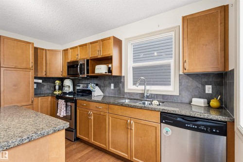 Kitchen featuring wood cabinetry, granite countertops, stainless steel appliances, and a tiled backsplash - 14807 141 Street, Edmonton, AB 
