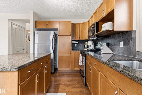 Well-appointed kitchen featuring wood-finish cabinetry, granite countertops, stainless steel refrigerator, built-in microwave, and a tile backsplash - 14807 141 Street, Edmonton, AB 