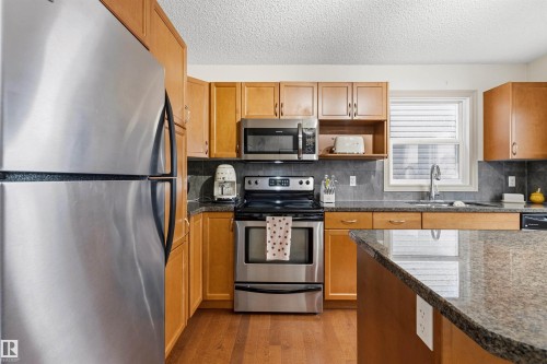 Kitchen featuring stainless steel appliances, wood-finish cabinetry, granite countertops, and a tile backsplash - 14807 141 Street, Edmonton, AB 