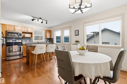 Kitchen and dining area featuring wood-finish flooring, light wood cabinetry, stainless steel appliances, and a kitchen island with a stone countertop - 14807 141 Street, Edmonton, AB 
