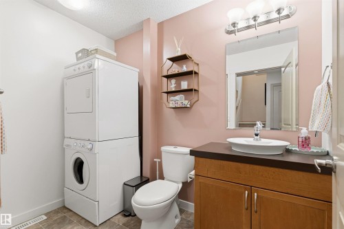Bathroom featuring a stacked washer and dryer, wood-finish vanity with a vessel sink, wall-mounted mirror, and overhead tri-bulb light fixture - 14807 141 Street, Edmonton, AB 