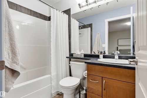 Bathroom featuring a white tub-shower combination with dark tile surround, a wood-finish vanity with a dark countertop, an undermount sink, and a large mirror - 14807 141 Street, Edmonton, AB 