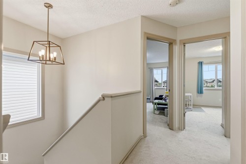 Upper-level landing featuring light-toned carpeting, neutral wall paint, and a contemporary linear chandelier - 14807 141 Street, Edmonton, AB 