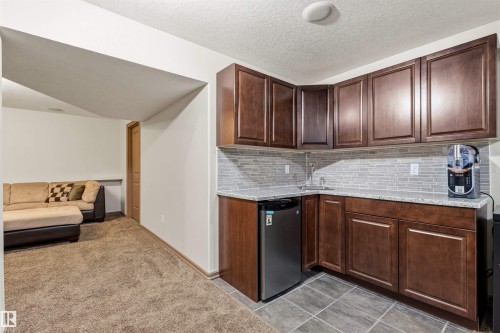 Wet bar featuring dark wood-finish cabinetry, light speckled countertops, and a subway tile backsplash - 14807 141 Street, Edmonton, AB 