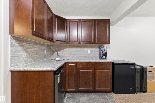 Wet bar featuring dark wood cabinetry, a light-toned countertop, and a tile backsplash - 14807 141 Street, Edmonton, AB 