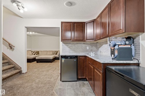 Wet bar featuring wood-finish cabinetry, light-toned countertop, and a mosaic tile backsplash - 14807 141 Street, Edmonton, AB 