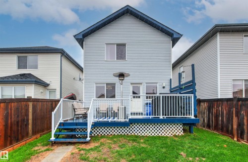 Rear exterior featuring a spacious deck with white railings and blue trim, a private fenced yard, light-colored siding, and a blue roofline - 14807 141 Street, Edmonton, AB 