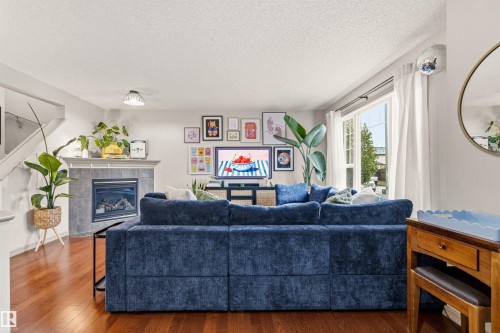 Living area featuring wood-finish flooring, a contemporary fireplace with a tiled surround and mantel, a large window with natural light, and a built-in staircase - 14807 141 Street, Edmonton, AB 