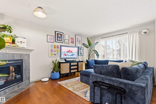 Living area featuring wood-finish flooring, a fireplace with a tiled surround and mantel, and a window with sheer white curtains - 14807 141 Street, Edmonton, AB 