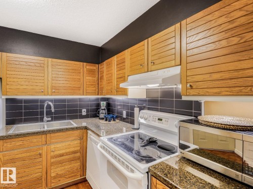 Kitchen featuring wood-finish cabinetry, dark subway tile backsplash, and stone countertops - 806 10149 Saskatchewan Drive, Edmonton, AB 