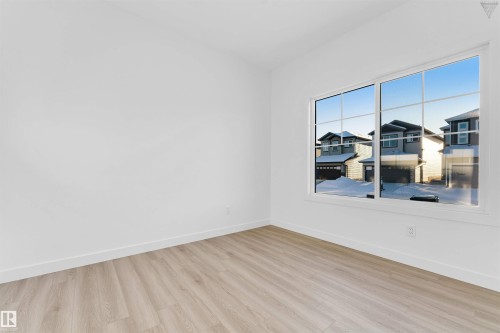Bright interior space featuring a large window with grid-pane detailing, light wood-finish flooring, white baseboards, and crisp white walls - 1224 14 Avenue Nw, Edmonton, AB - Indoor Photo Showing Other Room