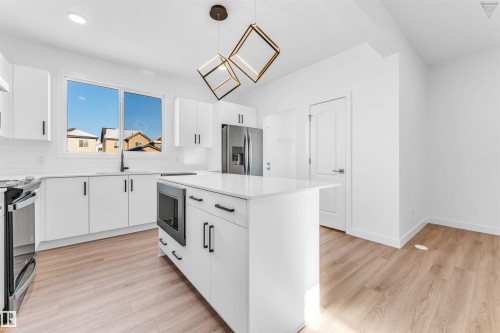 Contemporary kitchen featuring white cabinetry, a large window, a central island with an integrated microwave, stainless steel appliances, and light wood-finish flooring - 1224 14 Avenue Nw, Edmonton, AB - Indoor Photo Showing Kitchen With Upgraded Kitchen