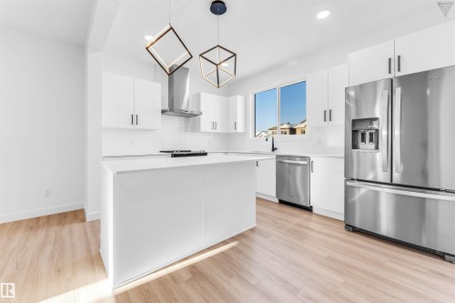 Modern kitchen featuring white cabinetry, stainless steel appliances, a center island with a solid surface countertop, wood-finish flooring, and contemporary pendant lighting fixtures - 1224 14 Avenue Nw, Edmonton, AB - Indoor Photo Showing Kitchen With Stainless Steel Kitchen With Upgraded Kitchen
