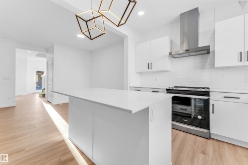 Modern kitchen featuring a central island with a quartz countertop, white cabinetry with black hardware, a stainless steel range hood, and a white subway tile backsplash - 1224 14 Avenue Nw, Edmonton, AB - Indoor Photo Showing Kitchen