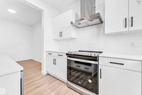 Modern kitchen featuring white shaker-style cabinetry, quartz countertops, a subway tile backsplash, stainless steel range hood, and wood-finish flooring - 1224 14 Avenue Nw, Edmonton, AB - Indoor Photo Showing Kitchen
