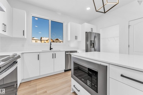 Modern kitchen featuring white cabinetry with black hardware, stainless steel appliances, light-toned wood-finish flooring, and a central island with an integrated microwave - 1224 14 Avenue Nw, Edmonton, AB - Indoor Photo Showing Kitchen With Stainless Steel Kitchen With Upgraded Kitchen