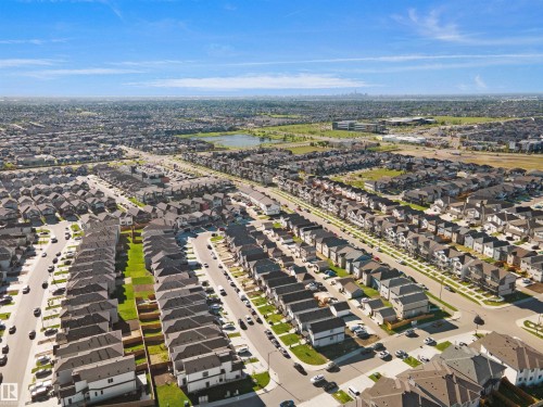 Expansive residential development featuring numerous single-family homes, a prominent street grid, and a distant park with a retention pond - 1224 14 Avenue Nw, Edmonton, AB - Outdoor With View