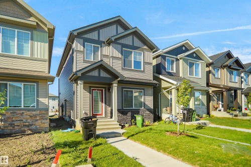 Two-story residence featuring a multi-toned facade with vertical and horizontal siding, stone accents, a covered front entry, and a red-framed front door - 1224 14 Avenue Nw, Edmonton, AB - Outdoor With Facade