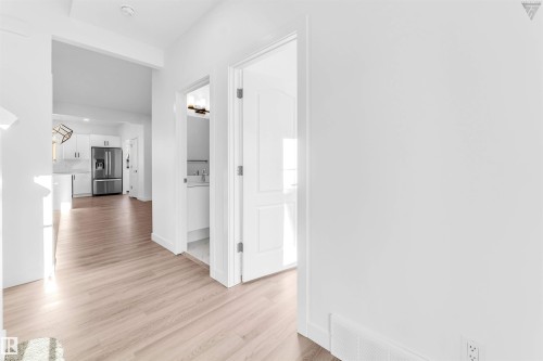 Light wood-finish flooring extending through an open doorway to a kitchen featuring white cabinetry and a stainless steel refrigerator - 1224 14 Avenue Nw, Edmonton, AB - Indoor Photo Showing Other Room