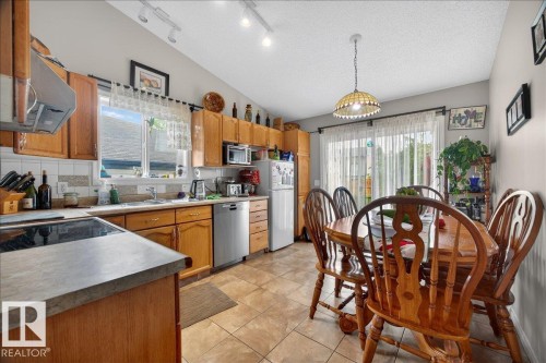 Kitchen featuring wood cabinetry, stainless steel appliances, and a tiled backsplash - 5108 138A Avenue, Edmonton, AB 