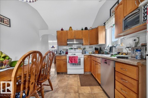 Kitchen featuring wood cabinetry, a white electric range, a stainless steel dishwasher, a single basin sink, and neutral-toned tiled flooring - 5108 138A Avenue, Edmonton, AB 