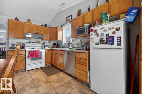 Kitchen featuring wood-finish cabinetry, white appliances, and a tile backsplash - 5108 138A Avenue, Edmonton, AB 