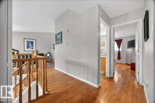 Upper-level hallway featuring wood-finish flooring, a wood staircase, light grey walls, and white trim - 5108 138A Avenue, Edmonton, AB 