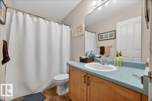 Bathroom featuring a single vanity with a light wood-finish cabinet and blue countertop, an undermount sink with chrome fixtures, a shower/tub combination with a white curtain, and ceramic tile flooring - 5108 138A Avenue, Edmonton, AB 