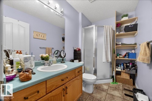 Bathroom featuring a light blue vanity countertop with an integrated sink, wood-finish cabinetry, and a mirrored wall - 5108 138A Avenue, Edmonton, AB 