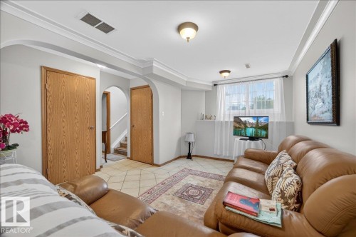 Spacious room featuring tile flooring, crown molding, arched doorways, a window with natural light, and overhead lighting fixtures - 5108 138A Avenue, Edmonton, AB 