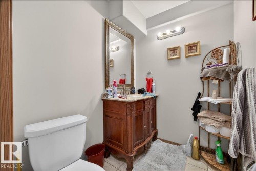 Bathroom featuring a vanity with a carved wood-finish base, a decorative framed mirror, and a white toilet - 5108 138A Avenue, Edmonton, AB 