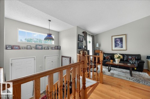 Open-concept living area with wood-finish flooring, featuring a partial staircase with wood railing, a transom window, and white interior doors - 5108 138A Avenue, Edmonton, AB 