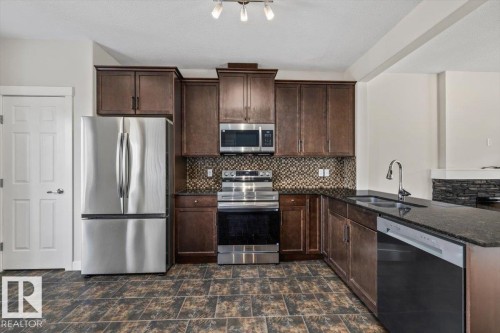 Kitchen featuring dark wood cabinetry, stainless steel appliances, a mosaic tile backsplash, dark stone countertops, and large format floor tiles - 356 Pioneer Road, Spruce Grove, AB 
