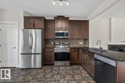 Kitchen featuring dark wood cabinetry, stainless steel appliances, a mosaic tile backsplash, dark stone countertops, and large format floor tiles - 